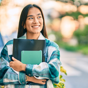 Woman holding notebooks outside smiling off into the distance