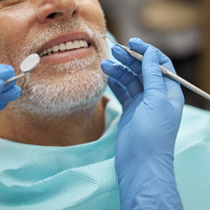 Blue gloved hands holding dental instruments to examine man’s mouth