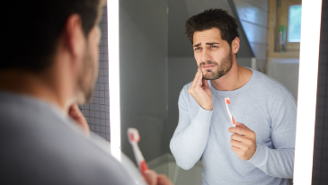 Man with toothbrush holding his face in pain