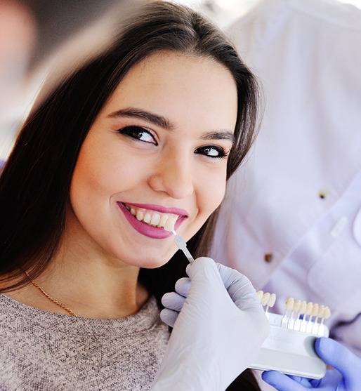 Dentist holding shade guide to patient’s teeth