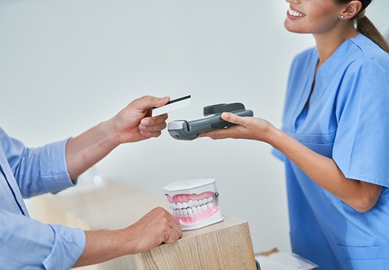 Woman in blue scrubs extending card reader to patient over desk with model teeth