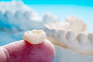 Close up of a tooth-colored crown resting on a fingertip