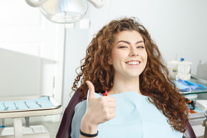 Woman with curly hair in dental chair giving thumbs up