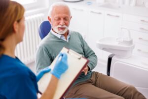 Dental team member taking notes during senior patient’s dental implant consultation 