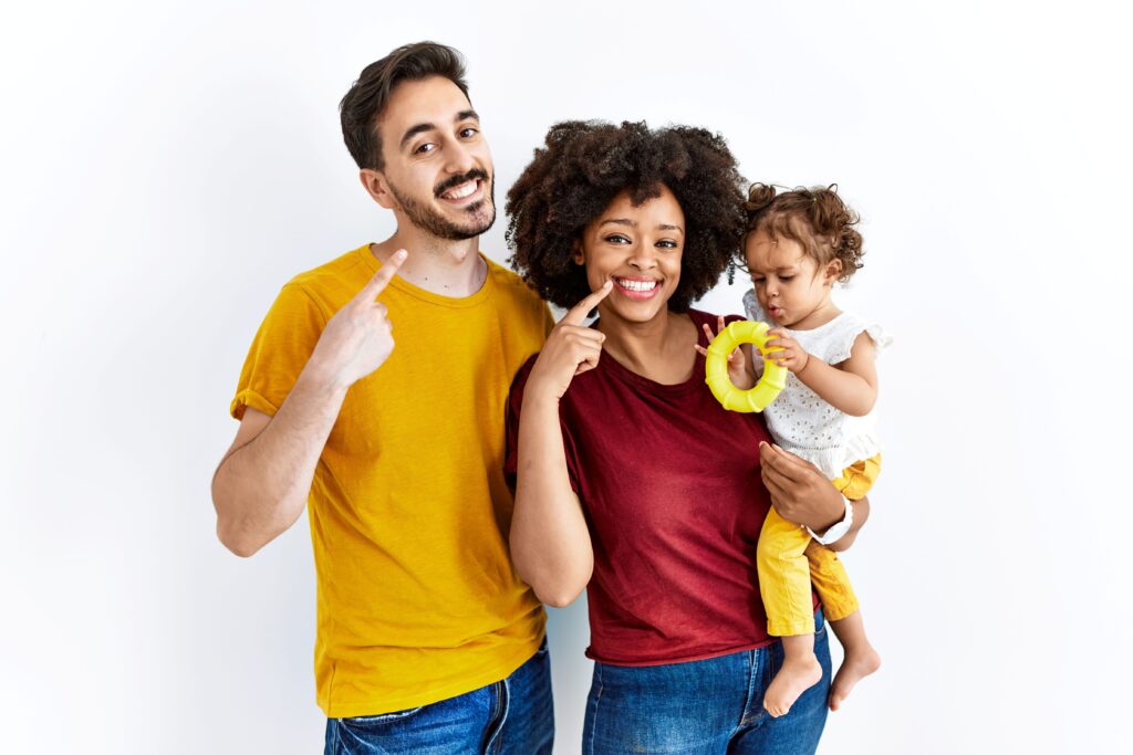 Man and woman holding small child pointing to their smiles